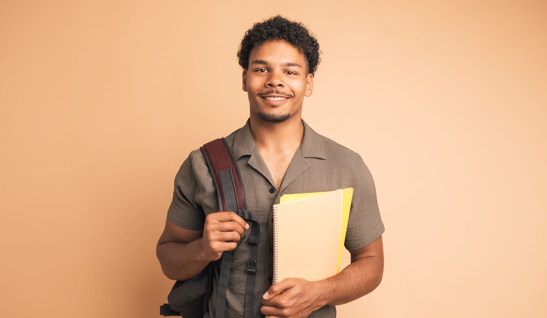 Heureux étudiant universitaire masculin avec sac à dos et livres dans un studio beige
