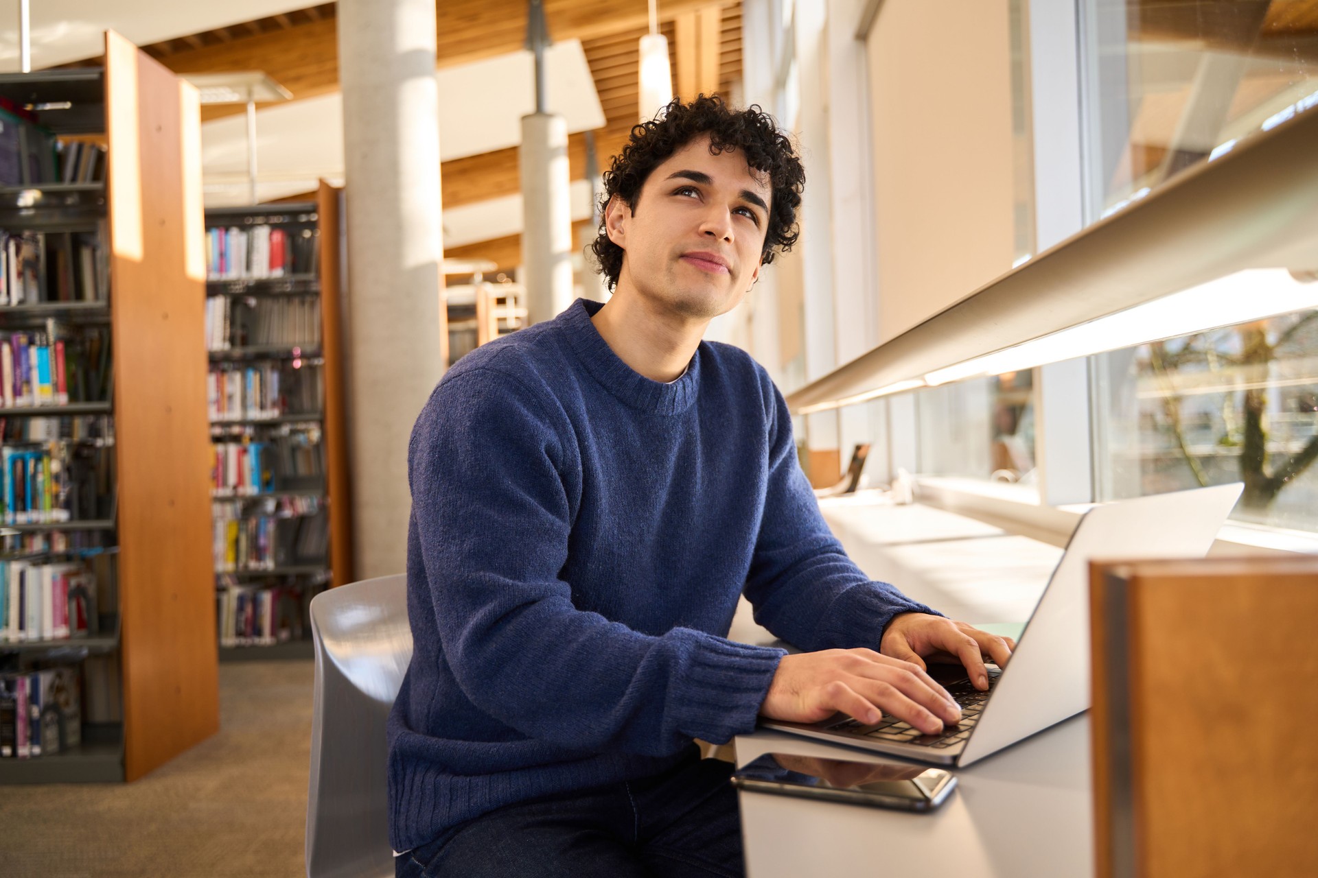 Pensée pensive d’un étudiant lorsqu’il travaille sur un ordinateur portable à la bibliothèque